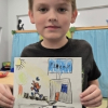 A boy presents his artwork depicting a gray building.