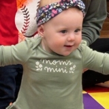 An infant in a green sweater dances at storytime in the library