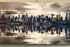 A city skyline with a golden white sky overhead, filled with several fluffy clouds. The scene is reflected perfectly at the horizon.