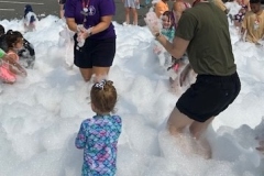 Youth Services Librarians Sara Figueroa and Stephanie Middleton join the children playing in foam in the library parking lot