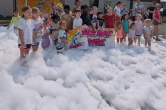Children stand knee deep in foam around a banenr that reads 'Best Summer Ever'