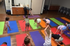 Librarian Stephanie leads a yoga lesson, demonstrating a pose in front of several young patrons.