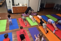 Librarian Stephanie leads a yoga lesson, demonstrating a pose in front of several young patrons.