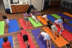 Librarian Stephanie leads a yoga lesson, demonstrating a pose in front of several young patrons.