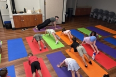 Librarian Stephanie leads a yoga lesson, demonstrating a pose in front of several young patrons.