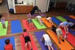 Librarian Stephanie leads a yoga lesson, demonstrating a pose in front of several young patrons.
